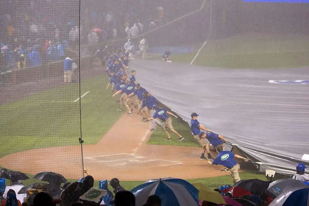 Employees pull a plastic tarp over the baseball field while it's raining.