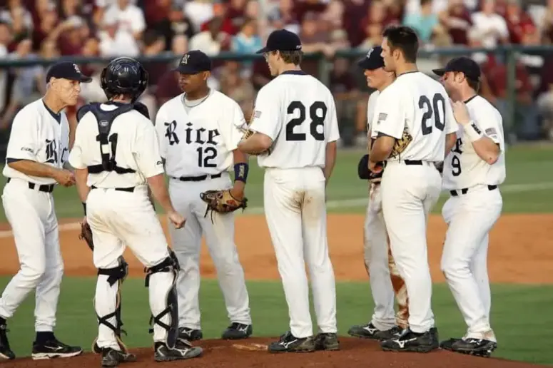 Baseball players in white long pants meet on the mound.