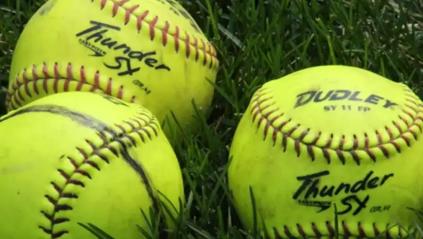 Three yellow softballs lying in the grass.