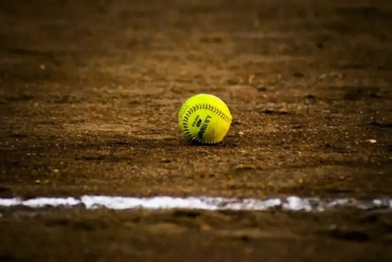 Yellow softball lying on the dirt infield.