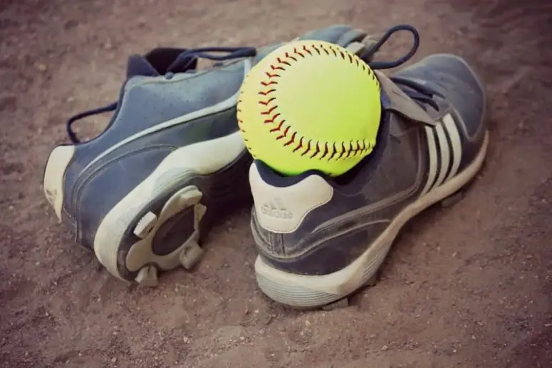 Softball cleats and softball lying on the ground.