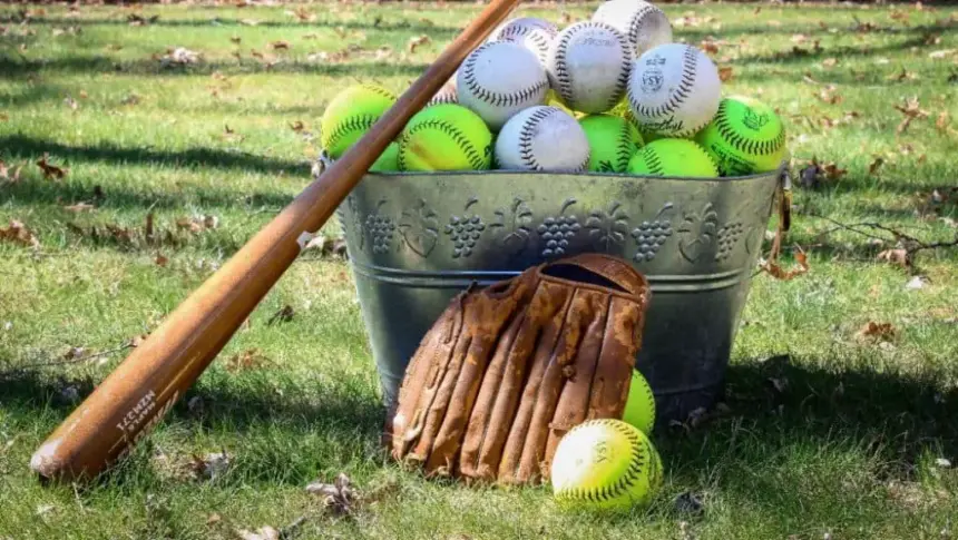Bucket full of baseball and softball balls, plus a glove and a bat.