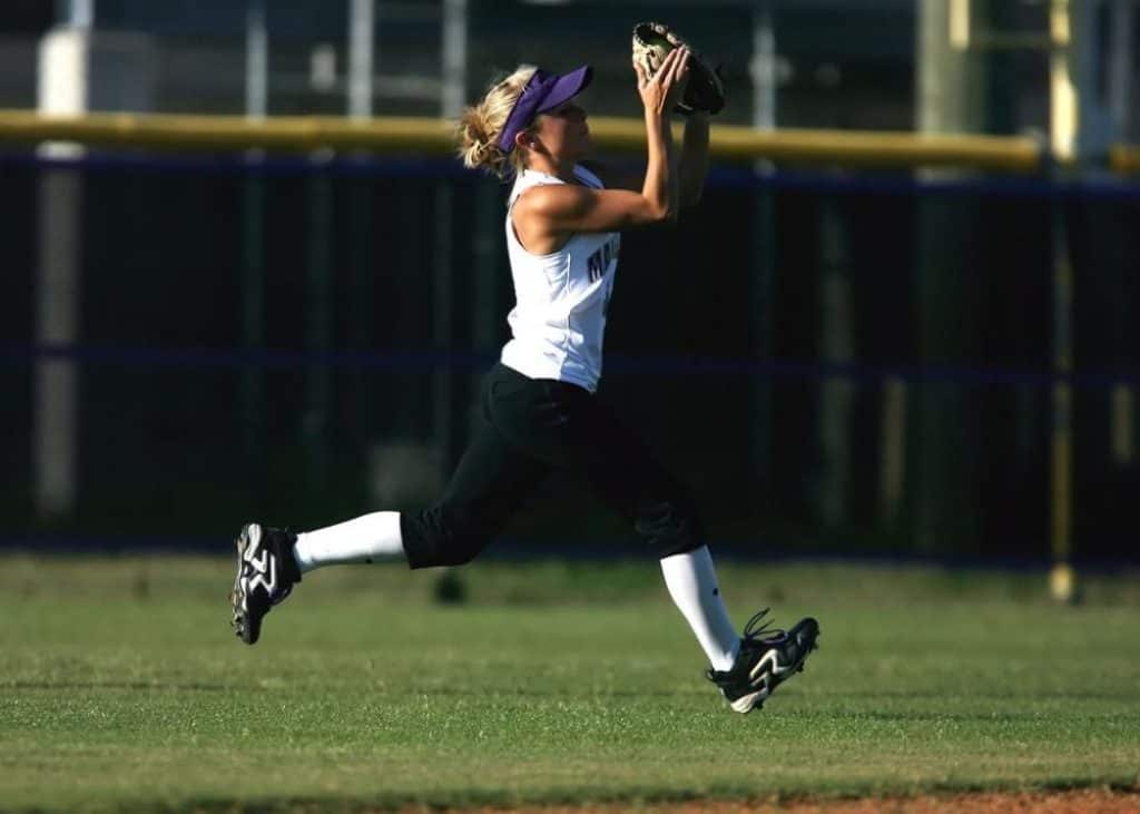 Female softball player running on grass field.