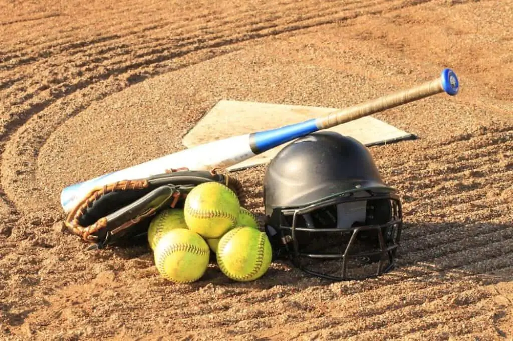 Softball helmet, balls, glove, and bat lying on the ground.