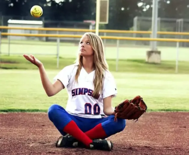 Girl sitting on the ground, playing with a softball.