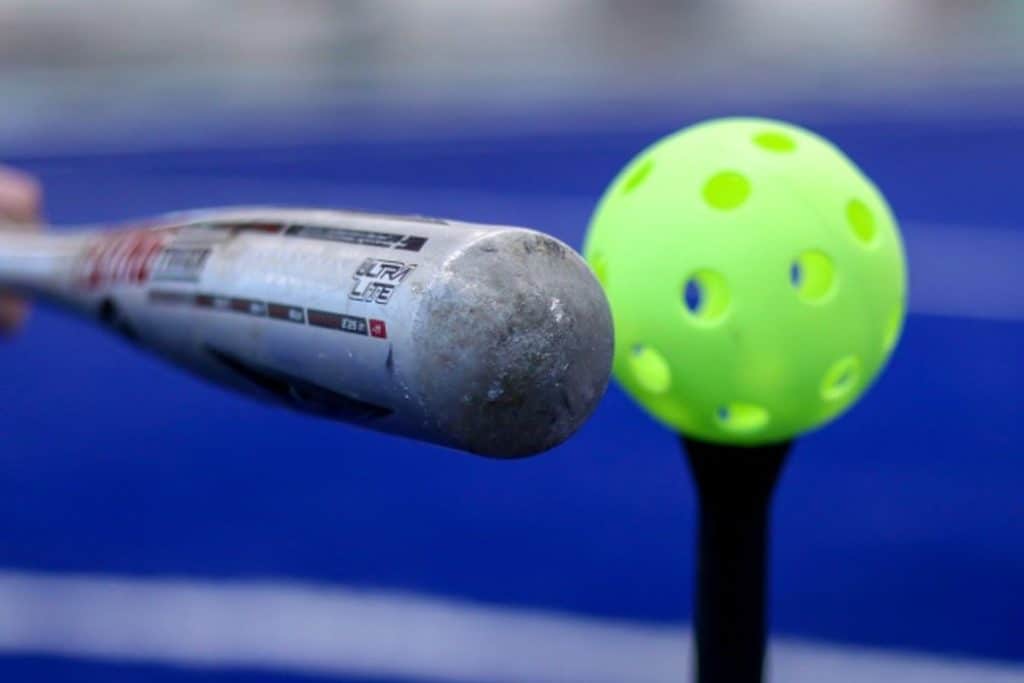 Baseball bat hitting a yellow wiffle ball.