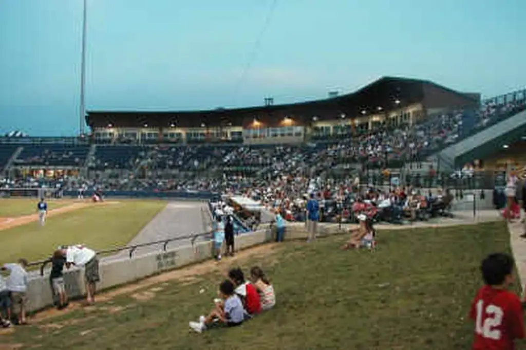People sit on the grass and watch the baseball game.