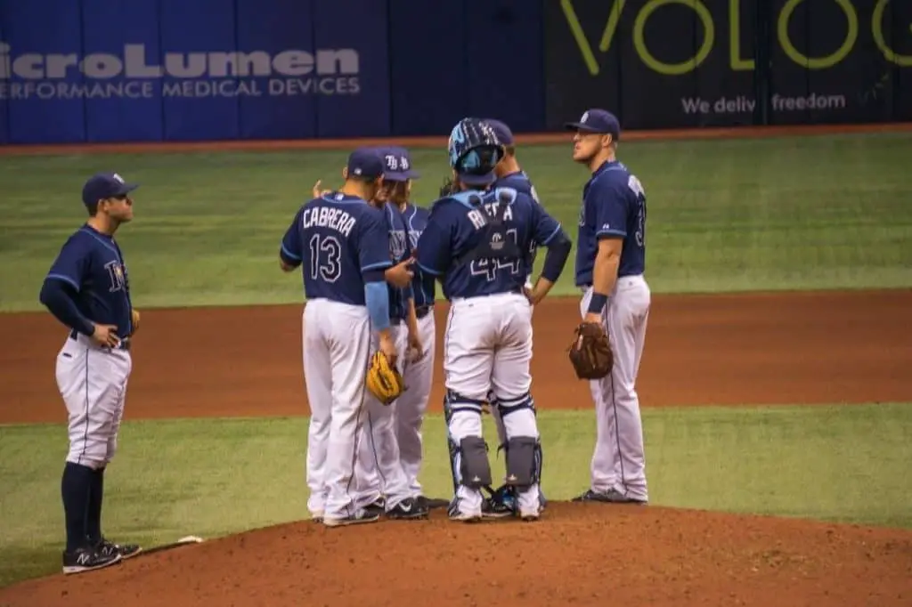 Baseball players in long pants meet at the mound.