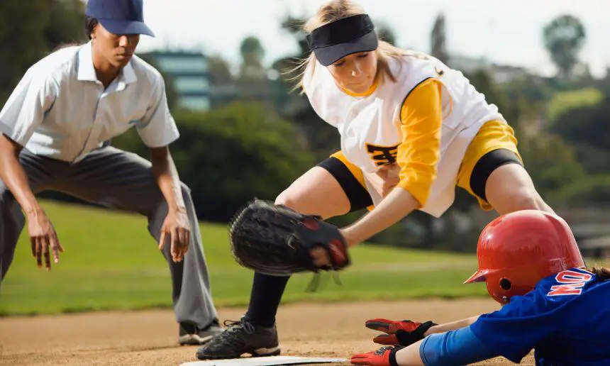 Female softball player sliding into the base with umpire watching.