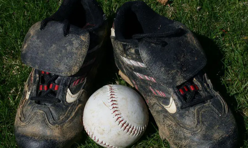 Baseball cleats with baseball lying on the green.