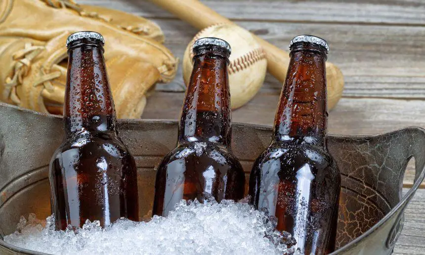 Bottles of beer on ice with baseball equipment in the background.